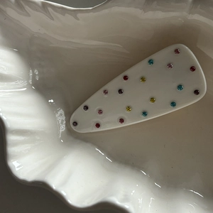 Detailed shot of multi-colored rhinestones on a white waterdrop hair clip in a shell tray
