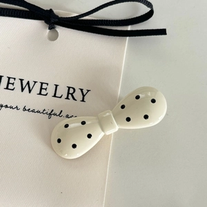 Détail de la pince à cheveux en acrylique crème à pois noirs sur carte bijoux