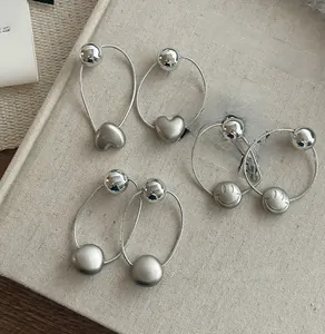 Détail de boucles d'oreilles en métal argenté avec breloques cœur et visage souriant
