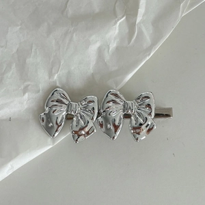 Barrette à cheveux double nœud en métal argenté poli sur fond blanc minimaliste