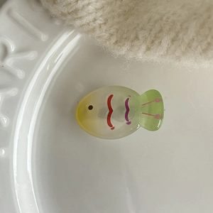 Macro view of transparent jelly-colored fish hair clip with green gradient on porcelain