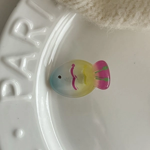 Detail view of a translucent fish-shaped hair clip with colorful resin gradient on a ceramic plate