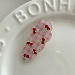 Détail d'une pince à cheveux rose à carreaux avec motif cerise et bords ondulés