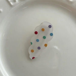 Détail d'une pince à cheveux nuage ondulé avec des pois colorés sur une assiette blanche