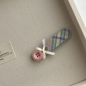 Detail of plaid fabric hair clip featuring pink button and white bow with heart charm
