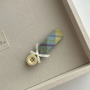 Close-up of plaid fabric hair clip with a white ribbon bow and button detail