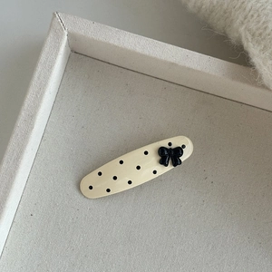 Beige polka dot hair clip with black bow on a minimalist canvas display tray