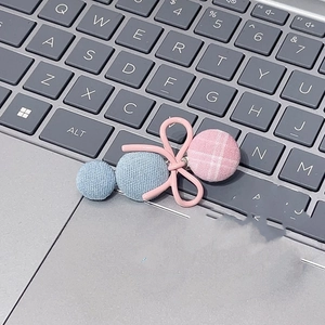 Detailed close-up of a pink plaid bow hair clip with blue knitted buttons on a keyboard