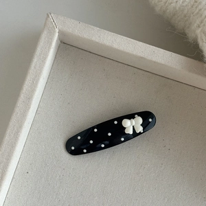 Polka dot hair clip with white bow accent on a soft textured cream fabric background