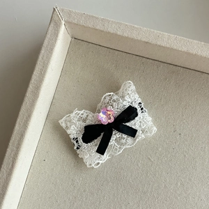Détail d'une pince à cheveux en dentelle blanche avec nœud noir et cristal rose fleuri