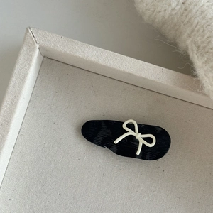 Detailed close-up of a black oval hair clip featuring a white minimalist bow design