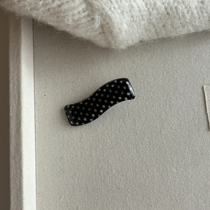 Elegant black polka dot acrylic hair clip with a smooth glossy finish on canvas background