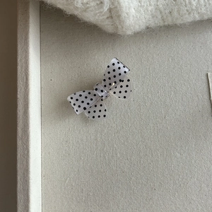 Detailed close-up of a semi-transparent white bow hair clip with classic black polka dots