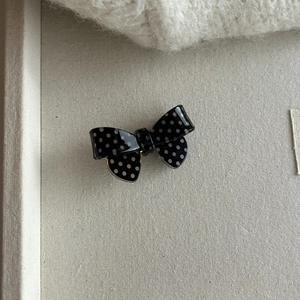 Detail of a black and white polka dot bow hair clip made of glossy acrylic on a soft tray