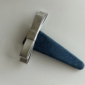 Silver metallic bow hair clip with dark blue denim fabric base on a white background