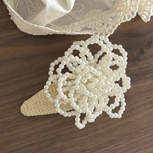 Elegant woven hair clip with white faux pearls on dark wood with lace background