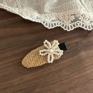 Detail of woven straw hair clip featuring white pearl flower on a rustic wood background