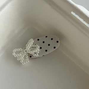 Barrette à cheveux avec nœud en perles et pois noirs sur tissu beige, vue sous un angle de 45°