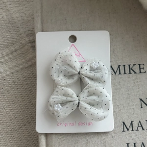 Detail view of two white polka dot chiffon bow hair clips with floral accents on a card