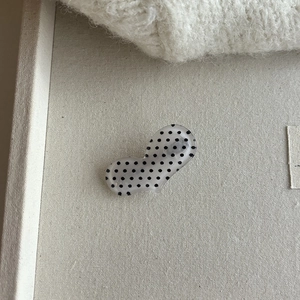 Detailed view of the light gray acrylic heart-shaped hair clip with vintage black polka dots