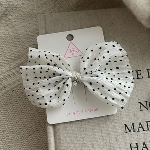 Detailed close-up of white chiffon polka dot hair bow with a pearl accent and brand card