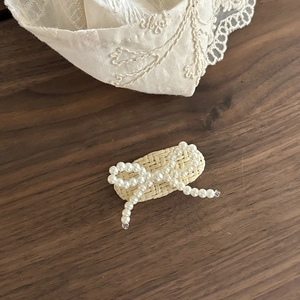 Detail of woven straw base hair clip with white faux pearl bow and elegant lace background