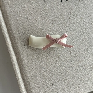 White wavy hair clip with pink ribbon bow on vintage beige textured book cover