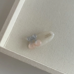 Détail de la pince à cheveux ovale crème avec nœud gris et perles cerises roses