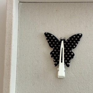 Elegant butterfly hair clip with black and white polka dots on a cream textured tray