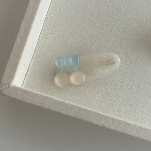 Détail de la pince à cheveux en résine crème avec nœud bleu et perles cerises roses