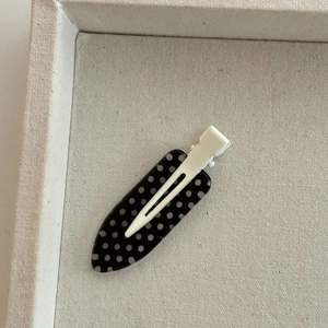 Close-up of black and white polka dot drop-shaped hair clip on cream fabric tray
