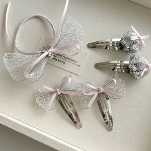 Girl's silver glitter bow hair clips and elastic hair tie set on a clean fabric background