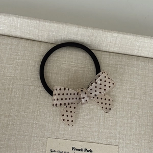 Close-up of a French style polka dot bow hair tie with a beige resin finish and black elastic