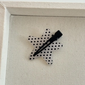 Detail of star-shaped hair clip with black polka dots on a matte black metal duckbill clip