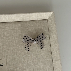 Detail of a sweet cream bow hair clip with black polka dots on a linen textured tray