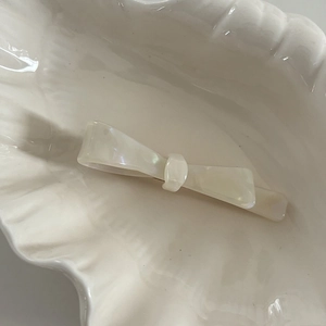 Elegant white acetate bow hair clip placed in a ceramic shell dish for daily styling