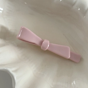 Detail view of pink acetic acid bow hair clip on a white ceramic shell tray