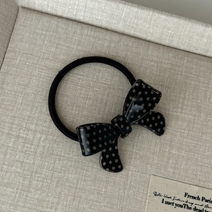 Detailed macro shot of a black polka dot bow elastic hair tie on a neutral background