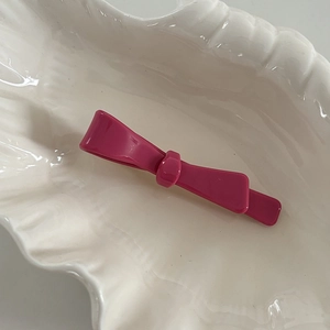 Close-up of a glossy rose red acetate bow hair clip placed on a white shell-shaped plate