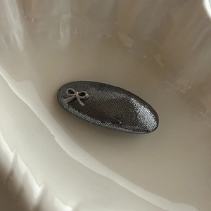 Barrette ovale gris foncé avec nœud argenté élégant posée dans un plat en céramique