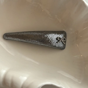 Détail d'une pince à cheveux argentée pailletée avec nœud sur plateau coquillage