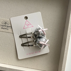 Detail of silver sequin pom-pom hair clips with pink bows on a white card