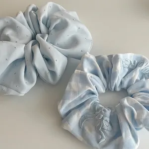 Light blue scrunchie set with bow embroidery and rhinestone details on gray background