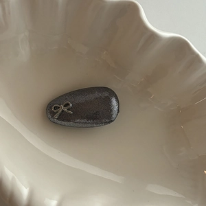 Vue macro d'une pince à cheveux en métal gris foncé avec nœud sur un plat coquillage