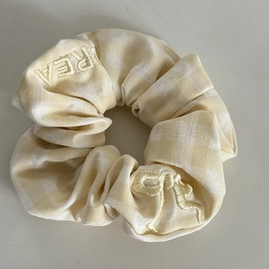 Detailed view of yellow plaid scrunchie with bow embroidery and text stitching