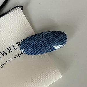 Detailed view of oval denim texture hair clip with polished dark blue resin finish