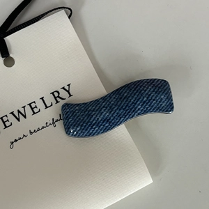 Close-up of wavy denim hair clip in deep blue denim fabric on white jewelry card