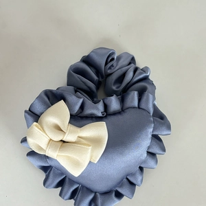 Close-up of heart-shaped blue satin scrunchie with white bow and ruffled edges