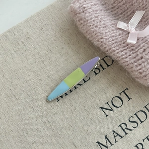 Detailed close-up of a three-color enamel duckbill hair clip on a beige linen background