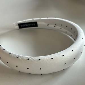 Detailed close-up of a thick white polka dot headband with a handmade label inside